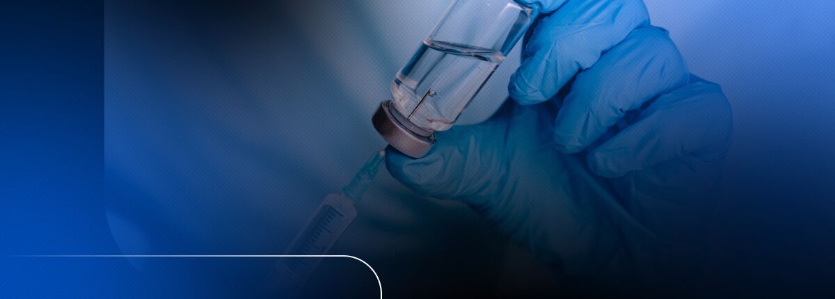 Frasco de vacina sendo segurado com luvas azuis