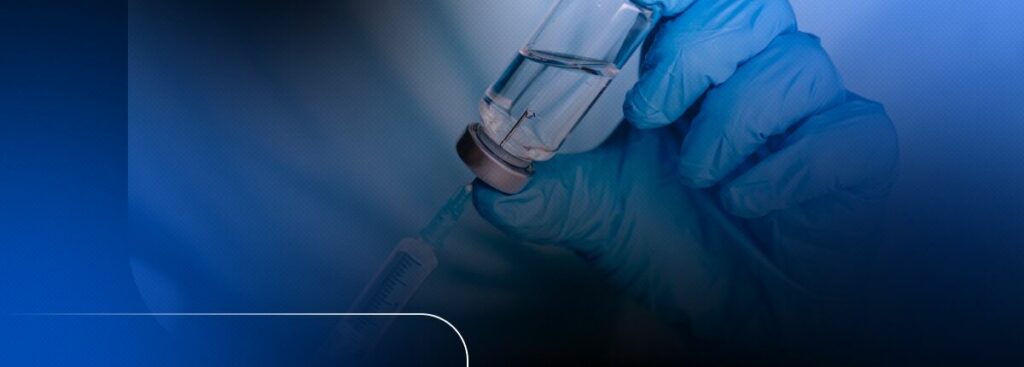 Frasco de vacina sendo segurado com luvas azuis